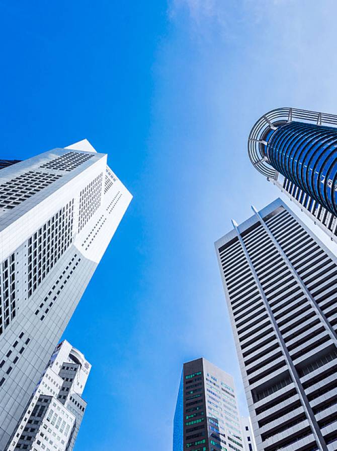 low-angle-modern-skyscrapers-glass-metallic-facades-blue-sky-singapore Low-angle view of modern skyscrapers with glass facades and metallic finishes against partly cloudy blue sky, highlighting vertical lines.